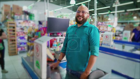 Foto de Empleado feliz del supermercado parado en la caja sonriendo a la cámara, Gerente de retratos de la tienda de comestibles brasileña sudamericana - Imagen libre de derechos