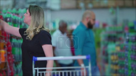 Foto de Consumidor femenino con carro que navega los estantes del supermercado, compradores en el pasillo de la tienda de comestibles que rasca para los productos - Imagen libre de derechos