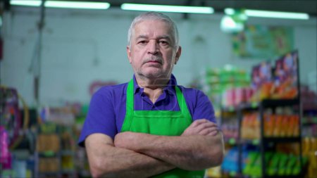 Photo for One serious older employee of grocery store crossing arms with stern worried expression stands inside supermarket local shop - Royalty Free Image