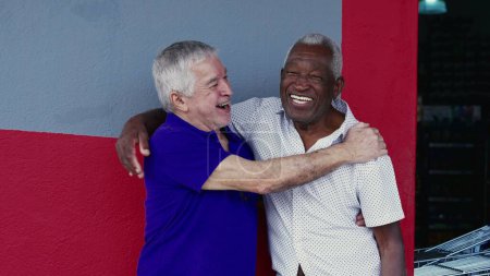 Authentische Interaktion zweier glücklicher älterer Freunde, die sich umarmen und mit High-Five feiern, draußen auf dem Gehweg stehen. Fröhliche Kameradschaft zwischen Afroamerikanern und Kaukasiern