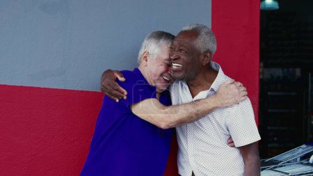 Foto de Authentic Interaction of Two Happy Diverse Older Friends, Hugging and Celebrating with High-Five, Standing Outside on Sidewalk (en inglés). Alegre compañía entre afroamericanos y caucásicos - Imagen libre de derechos