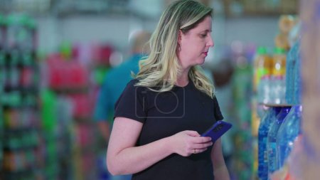 Téléchargez les photos : Femme avec téléphone, Liste d'achats dans Supermarché Soda Aisle - en image libre de droit