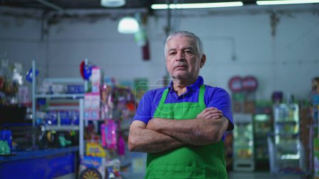 Téléchargez les photos : Gestionnaire de supermarché sérieux avec bras croisés, expression préoccupée de l'ancien propriétaire de petite entreprise à l'intérieur du magasin - en image libre de droit