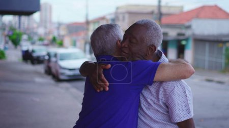 Foto de Dos viejos amigos diversos intercambian abrazos en el entorno urbano. Hombre afroamericano abrazando a su amigo caucásico que representa una escena de amistad y camaradería en la calle - Imagen libre de derechos