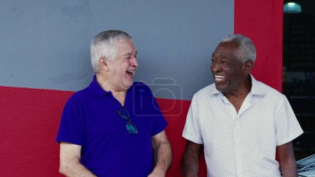 Photo for Authentic Interaction of Two Happy Diverse Older Friends, Hugging and Celebrating with High-Five, Standing Outside on Sidewalk. Cheerful Companionship Between African American and Caucasian Individuals - Royalty Free Image