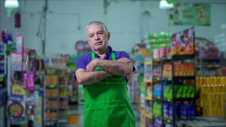 Photo for One serious older employee of grocery store crossing arms with stern worried expression stands inside supermarket local shop - Royalty Free Image