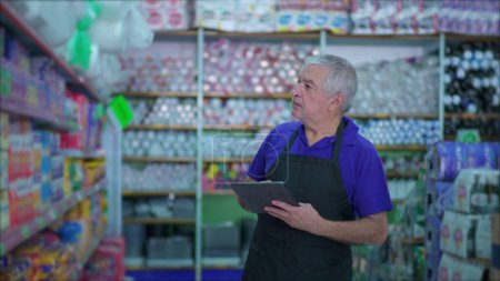 Téléchargez les photos : Directeur principal de l'épicerie vérifier l'inventaire des produits sur étagère avec dispositif de table, employé caucasien masculin inspectant les articles au rayon du supermarché - en image libre de droit