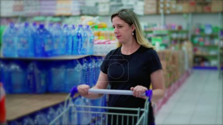 Foto de Mujer caucásica de mediana edad comprando en el pasillo del supermercado con la cesta, examinando productos - Imagen libre de derechos