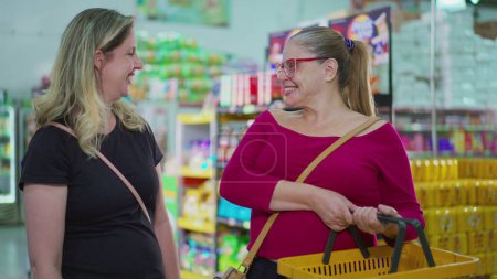 Foto de Dos alegres compradores femeninas sonriendo a la cámara dentro de la tienda de supermercados sosteniendo la cesta en la mano. Rostros de retratos de mujeres sonrientes de mediana edad haciendo compras de comestibles - Imagen libre de derechos