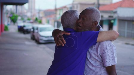 Foto de Dos viejos amigos diversos intercambian abrazos en el entorno urbano. Hombre afroamericano abrazando a su amigo caucásico que representa una escena de amistad y camaradería en la calle - Imagen libre de derechos
