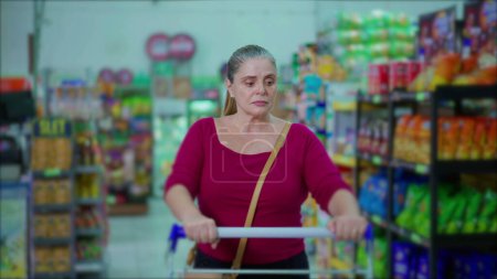 Téléchargez les photos : Femme d'âge moyen Navigation sur les produits en Supermarché allée - en image libre de droit