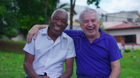 Photo for Older Caucasian and African American Friends Share Happy Moment on Park Bench laughing and smiling together. Friend putting arm around companion - Royalty Free Image