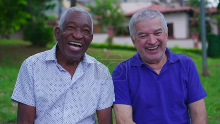Foto de Dos alegres amigos mayores Diversos riendo y sonriendo juntos en el banco del parque al aire libre. Felicidad en la vejez años de jubilación. Retrato del pueblo brasileño - Imagen libre de derechos