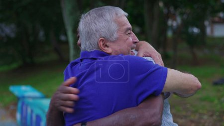 Foto de Dos amigos diversos abrazándose en el parque. Un hombre mayor afroamericano abrazando a un compañero caucásico que representa amistad y camaradería en la vejez - Imagen libre de derechos