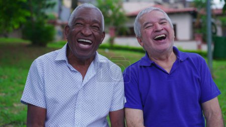 Téléchargez les photos : Deux amis aînés joyeux et diversifiés riant et souriant ensemble sur le banc du parc à l'extérieur. Bonheur dans les années de retraite vieillesse. Portrait du peuple brésilien - en image libre de droit