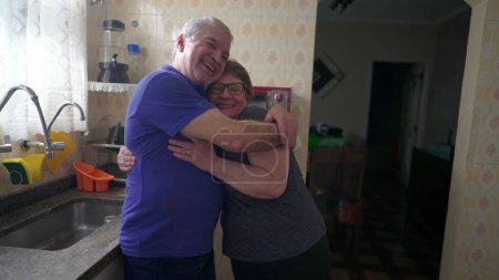 Photo for Senior couple loving embrace standing in home kitchen, causal authentic real life married man and woman hug, husband with arm around wife - Royalty Free Image
