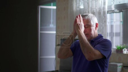 Photo for Candid Devout Senior person Praying to God at home kitchen. Authentic Spiritual scene of a hopeful Elderly man asking for divine HELP and SUPPORT - Royalty Free Image