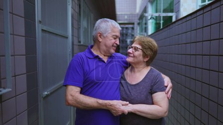 Téléchargez les photos : Couple aîné embrassant dans l'étreinte aimante debout dans la résidence arrière-cour. Sud-Américain âgé marié mari et femme - en image libre de droit