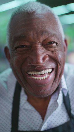 Photo for Portrait of a happy Elderly African American Man with Gray Hair and Wrinkles, Wearing Black Apron, smiling at camera with joyful expression. Charismatic and friendly employee person - Royalty Free Image