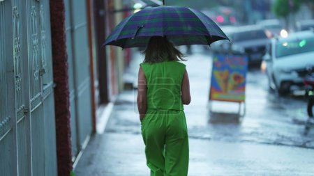 Foto de Vista trasera de la persona caminando bajo la lluvia sosteniendo el paraguas - Imagen libre de derechos