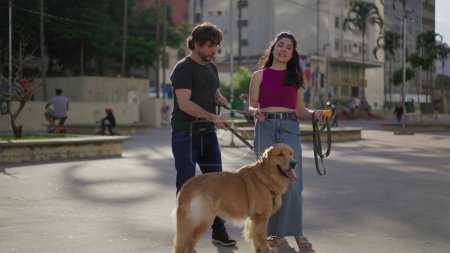 Téléchargez les photos : Couple dans le parc avec leur chien amical profiter de la brise du week-end et bavarder - en image libre de droit