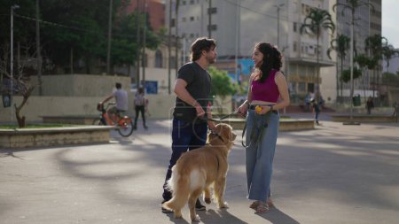 Téléchargez les photos : Couple dans le parc avec leur chien amical profiter de la brise du week-end et bavarder - en image libre de droit