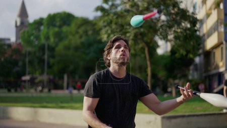 Téléchargez les photos : Homme Juggler artiste démontrant ses compétences à l'extérieur dans le parc urbain de la ville. Personnage artiste jongler avec des objets dans l'air - en image libre de droit
