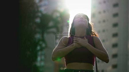 One Spiritual young woman standing outdoors looking up at sky feeling hopeful. Faithful person feeling the presence of God in nature sunlight