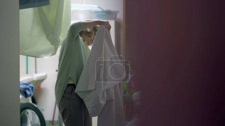 Photo for One senior woman ironing clothes standing in laundry room. Candid older person doing domestic everyday chores at home. Authentic domesticity - Royalty Free Image