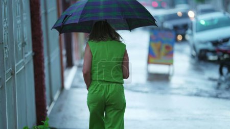 Photo for Back view of person walking in the rain holding umbrella - Royalty Free Image