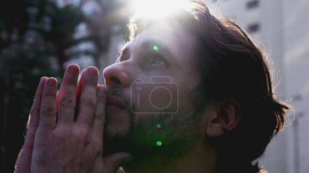 Photo for Faithful young man looking up at sky in prayer asking for God_s help with hopeful expression. A Spiritual male person in 30s with lens flare sunlight - Royalty Free Image