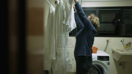 Photo for Candid older lady putting clothes to dry on laundry rack. Real life domestic scene of senior person doing household routine - Royalty Free Image