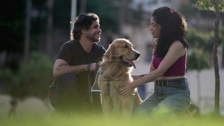 Téléchargez les photos : Couples sincères profitant de la journée d'été au parc avec leur Golden Retriever Pet au soleil - en image libre de droit