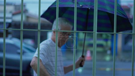 Téléchargez les photos : Homme mûr âgé se préparant pour une promenade dans la soirée pluvieuse, ouverture parapluie sur le trottoir de la rue - en image libre de droit