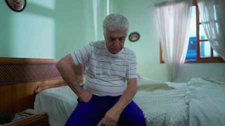 Téléchargez les photos : Homme âgé réfléchi réfléchissant à la décision, assis au chevet du lit dans la sombre contemplation de la chambre - en image libre de droit
