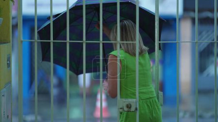 Téléchargez les photos : Femme face à la pluie, ouverture parapluie, quitter la maison et marcher dans le trottoir de la rue - en image libre de droit