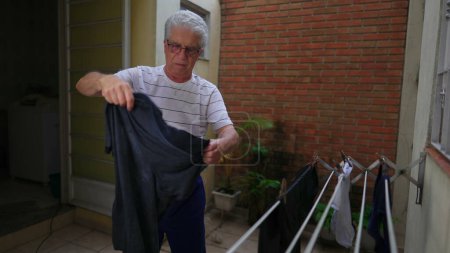 Photo for Senior man doing laundy and putting clothes to dry on hanger. Older person squeezing wet shirt removing water residue, doing domestic household chore activity - Royalty Free Image