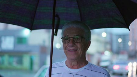 Téléchargez les photos : Happy Senior Homme se promène dans la ville trottoir tenant parapluie pendant la journée de pluie - en image libre de droit