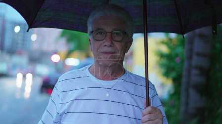Photo for Senior man walks forward holding umbrella during rainy day. One caucasian elderly mature person strolling in city sidewalk - Royalty Free Image