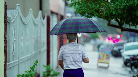 Foto de El hombre mayor que sale de casa mientras llueve, abre el paraguas y cierra la puerta detrás de él. Senderos en la acera de la calle - Imagen libre de derechos