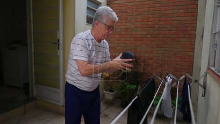 Photo for Senior man doing laundy and putting clothes to dry on hanger. Older person squeezing wet shirt removing water residue, doing domestic household chore activity - Royalty Free Image