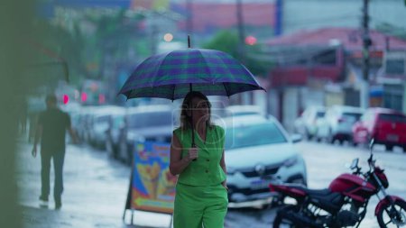 Téléchargez les photos : Femme face à la pluie pendant l'après-midi pluvieux dans la rue de la ville. Personne contemplative marchant tenant parapluie - en image libre de droit