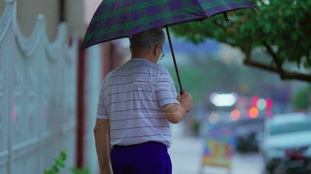 Foto de Personas mayores caucásicas saliendo de casa y caminando en la calle con paraguas durante la lluvia - Imagen libre de derechos