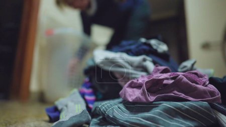 Photo for Domestic scene of person doing laundry. Close-up of clothes stacked together on floor with person blurred in background doing household routine - Royalty Free Image