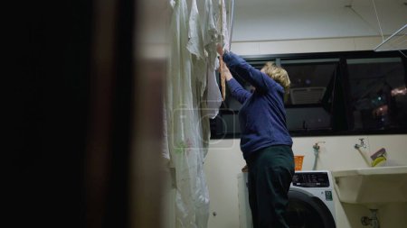 Photo for Senior woman tending to laundry on drying rack, a glimpse into daily life. Domestic routine scene of retired older lady at home. Candid and authentic - Royalty Free Image