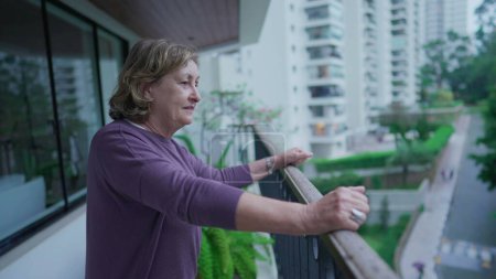 Foto de Feliz mujer mayor de pie en el balcón saludando a la gente en el barrio. Alegre señora mayor en los años 70 disfrutando de la jubilación - Imagen libre de derechos