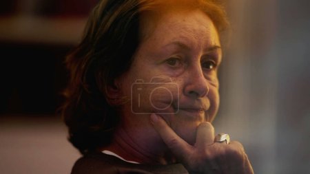 Photo for One pensive senior woman lost in thought. A contemplative older lady seen through window reflection in the evening - Royalty Free Image