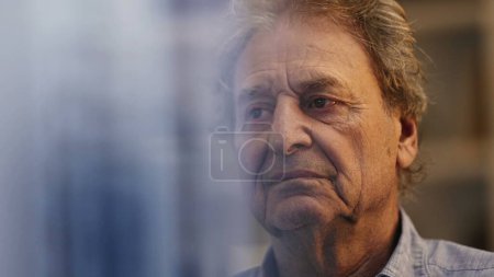 Photo for One serious contemplative senior man thinking about life seen through window reflection. Mediative wrinkled older male person in 70s at night - Royalty Free Image