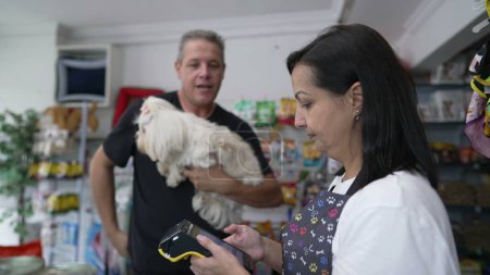 Photo for Happy Client Pays for Grooming Procedure, Contactless Payment at Pet Shop with Small Dog in Hand - Royalty Free Image