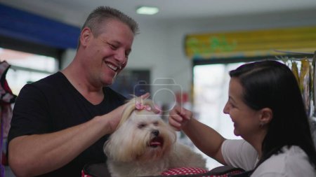 Foto de Happy Pet Client Holding Small Dog. Propietaria de una empresa femenina entregando Shih-Tzu al hombre después del baño de aseo - Imagen libre de derechos